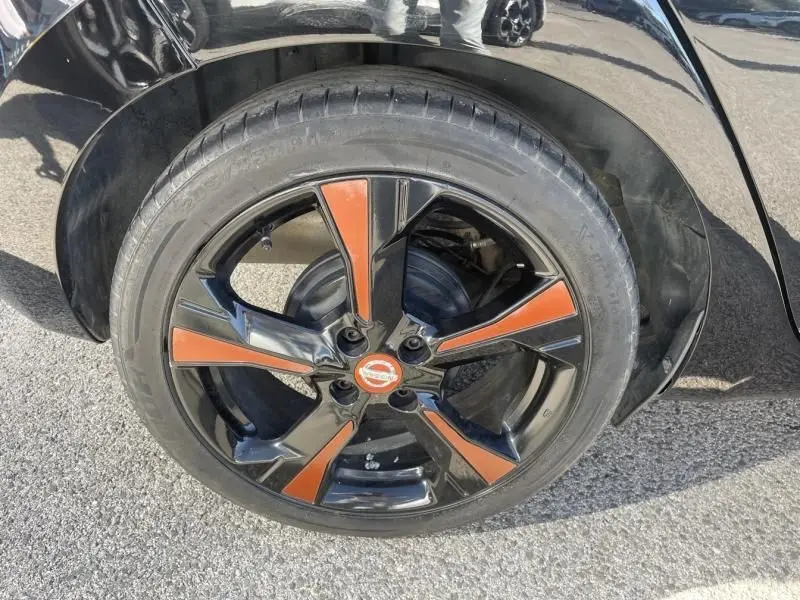 Gros plan sur la roue avant gauche noire d'une Nissan Micra 2017, jante noire avec inserts orange et logo Nissan central.
