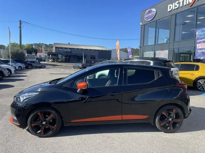 Vue latérale droite d'une Nissan Micra noire 2017 avec détails orange sur les jantes et les rétroviseurs, stationnée en extérieur.