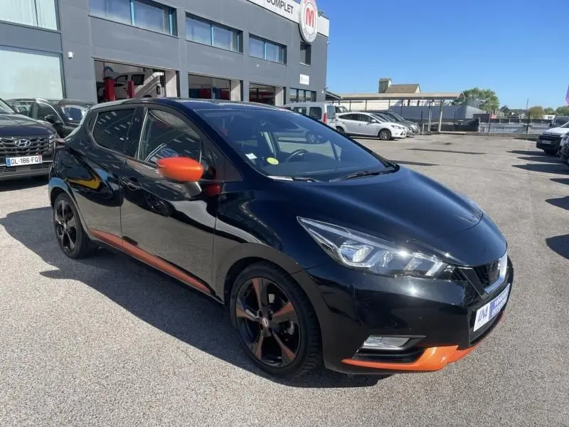 Nissan Micra 1.5 DCI 90 N-Connecta noire vue 3/4 avant droit avec détails orange sur rétroviseurs et bas de caisse.