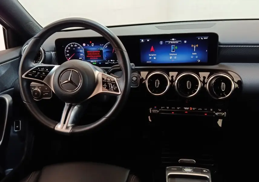 Vue intérieure du tableau de bord et volant cuir Mercedes GLA 250 e 2023 avec écran tactile large et aérateurs ronds chromés.