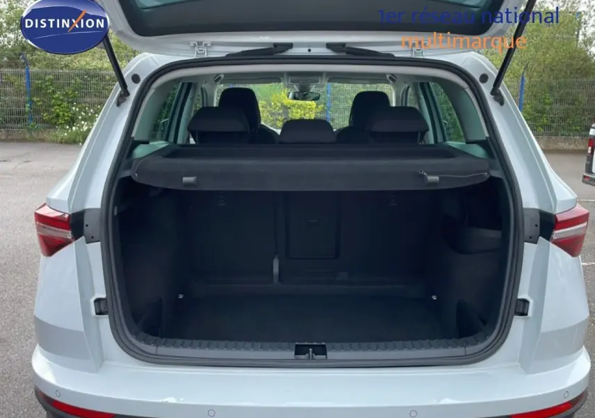 Vue arrière ouverte du coffre d'un Skoda Karoq blanc glacier 2025, montrant l'espace de chargement et la plage arrière noire.
