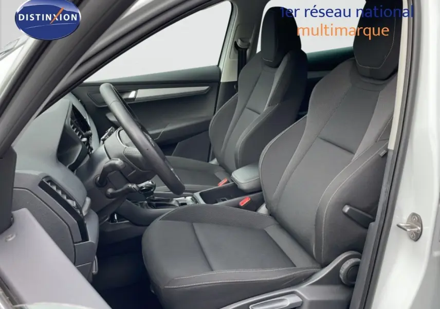 Vue intérieure côté conducteur du Skoda Karoq blanc glacier 2025, sièges tissu gris avec coutures contrastées.