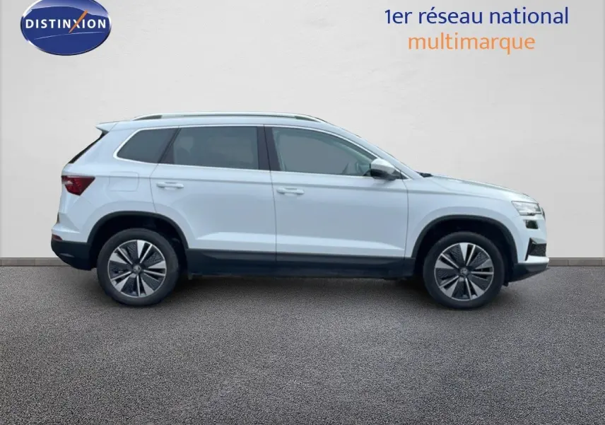 Vue de profil côté gauche d’un Skoda Karoq blanc glacier 2025 avec jantes bi-ton et barres de toit.