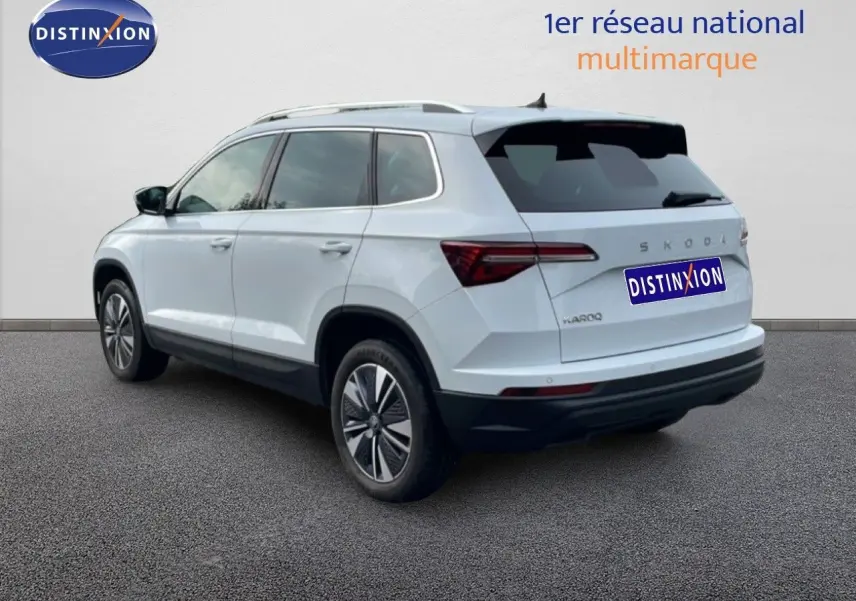 Vue 3/4 arrière droite d'un Skoda Karoq blanc glacier, SUV compact avec jantes bi-ton et feux arrière LED.