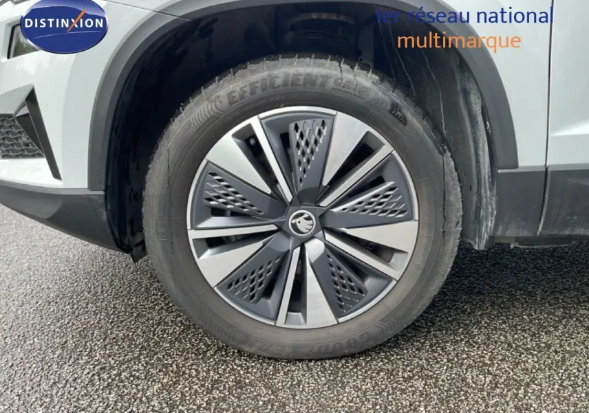 Gros plan sur la roue avant droite d’un Skoda Karoq blanc glacier, mettant en valeur la jante alliage au design moderne.
