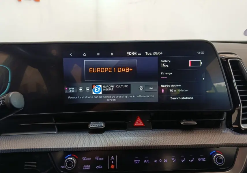 Vue rapprochée du tableau de bord tactile du Kia Sportage blanc 2022, affichant la radio et l'état de la batterie.