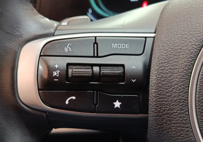 Gros plan sur les commandes multifonctions noires du volant cuir du Kia Sportage hybride rechargeable 2022.