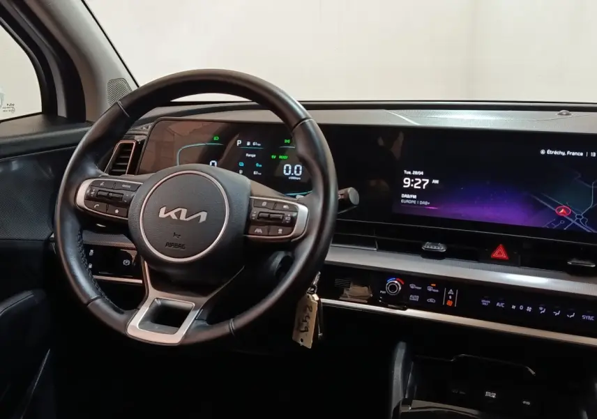 Intérieur du Kia Sportage 2022 vu du poste de conduite, volant cuir multifonctions et grand écran tactile central allumé.