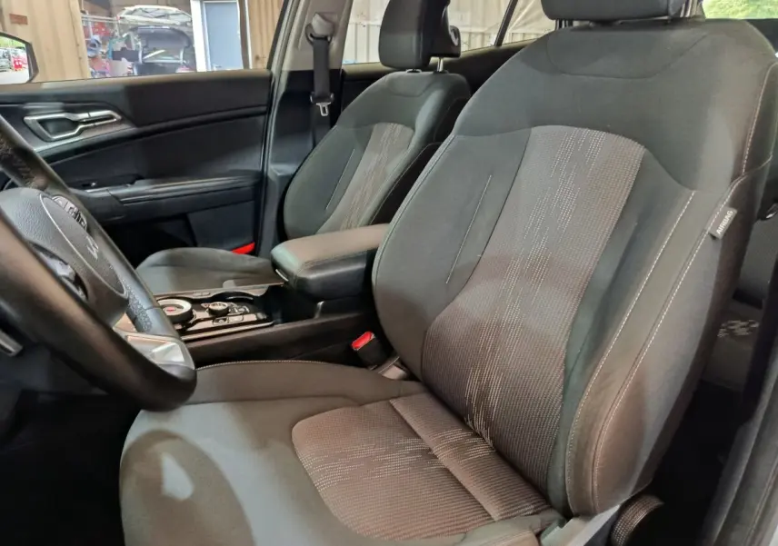Vue intérieure côté conducteur du Kia Sportage 2022, sièges tissu gris avec accoudoir central noir.