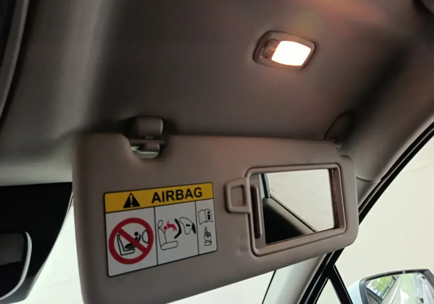 Détail intérieur du pare-soleil côté conducteur du Kia Sportage blanc 2022 avec miroir et avertissement airbag visible.