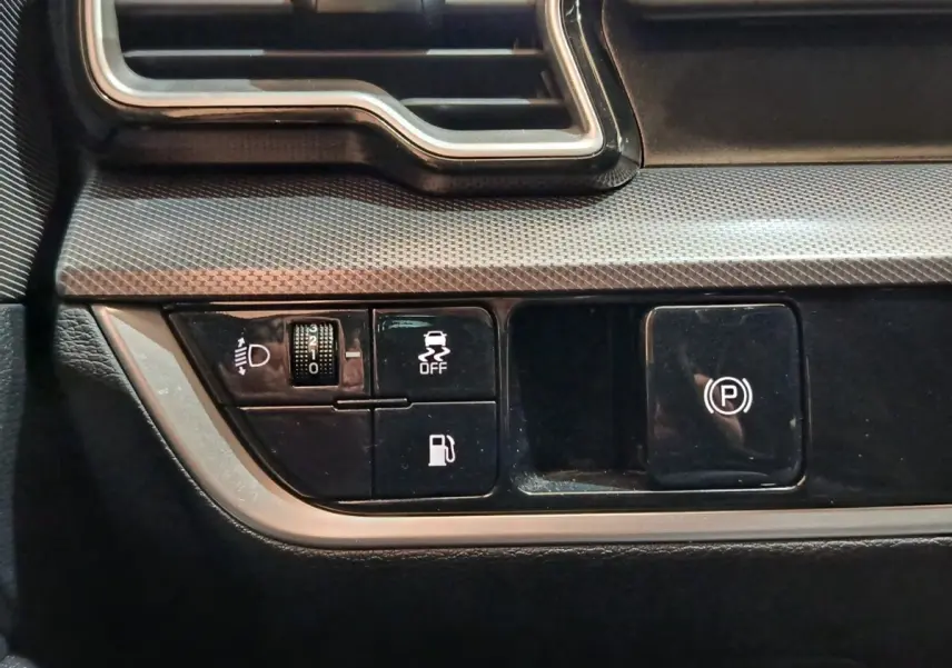 Gros plan sur les commandes de tableau de bord noir du Kia Sportage blanc, avec bouton frein à main électrique et réglage phares.