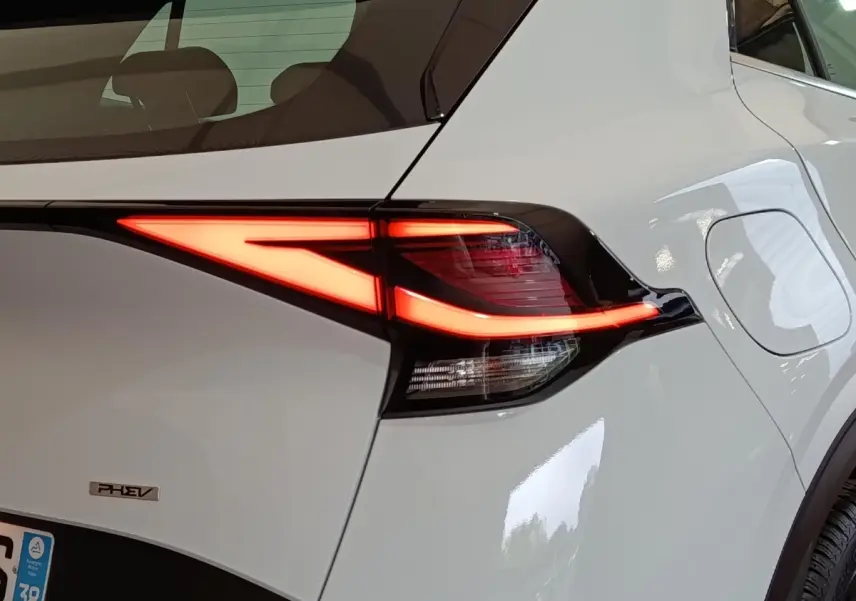 Gros plan sur le feu arrière droit allumé d’un KIA Sportage blanc hybride rechargeable avec logo PHEV visible.