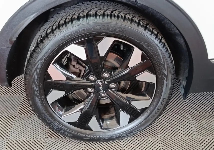 Gros plan sur la roue avant droite du KIA SPORTAGE blanc avec jante alliage noire et argentée, pneu Nokian.