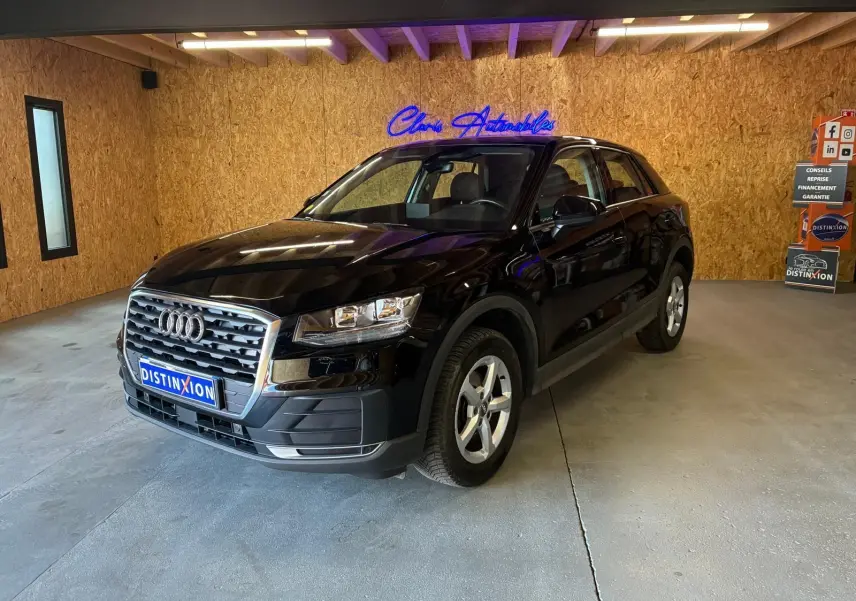 Audi Q2 noir vue 3/4 avant droit dans un showroom avec calandre chromée et jantes argentées.