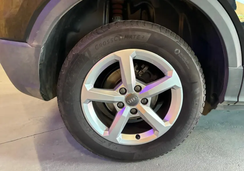 Gros plan sur la roue avant droite d’un Audi Q2 noir, mettant en valeur la jante argentée à cinq branches.