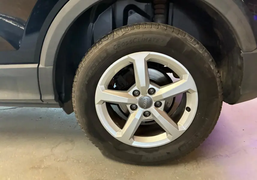 Gros plan sur la roue avant droite d’un Audi Q2 noir, mettant en valeur la jante argentée à cinq branches.