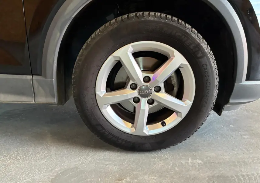 Gros plan sur la roue avant droite d’un Audi Q2 noir, mettant en valeur la jante argentée à cinq branches et le pneu Michelin.