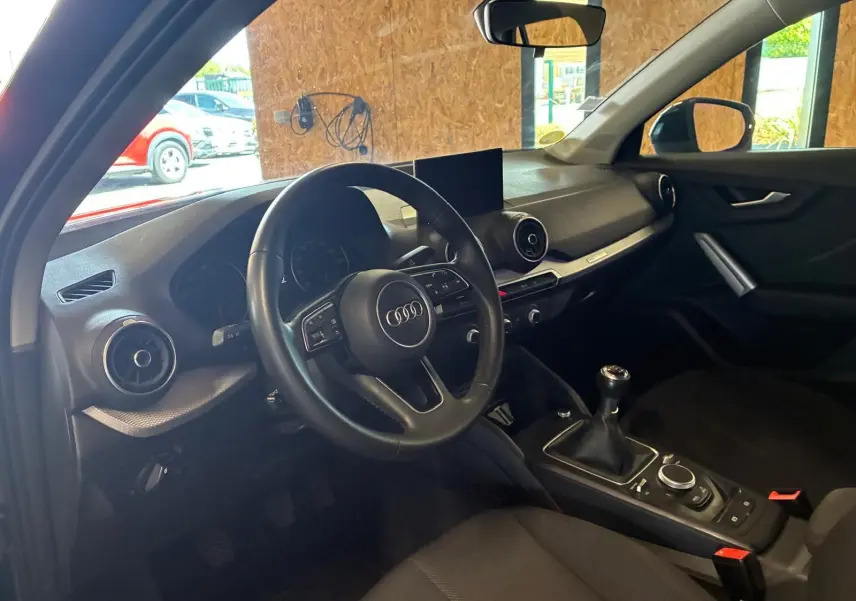 Intérieur noir de l'Audi Q2 30 1.6 TDI 2020 vu côté conducteur, volant multifonction et boîte manuelle visibles.