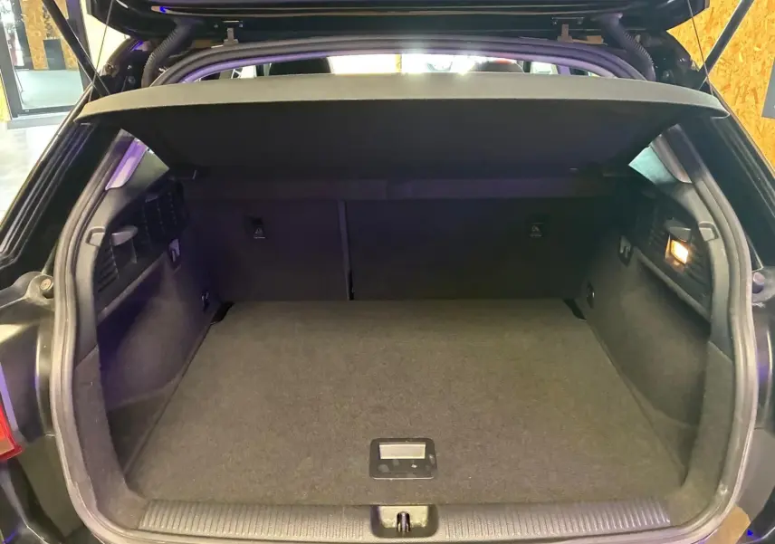 Coffre ouvert vu de l'arrière d'un Audi Q2 noir, montrant un espace de chargement propre et vide avec cache-bagages en place.