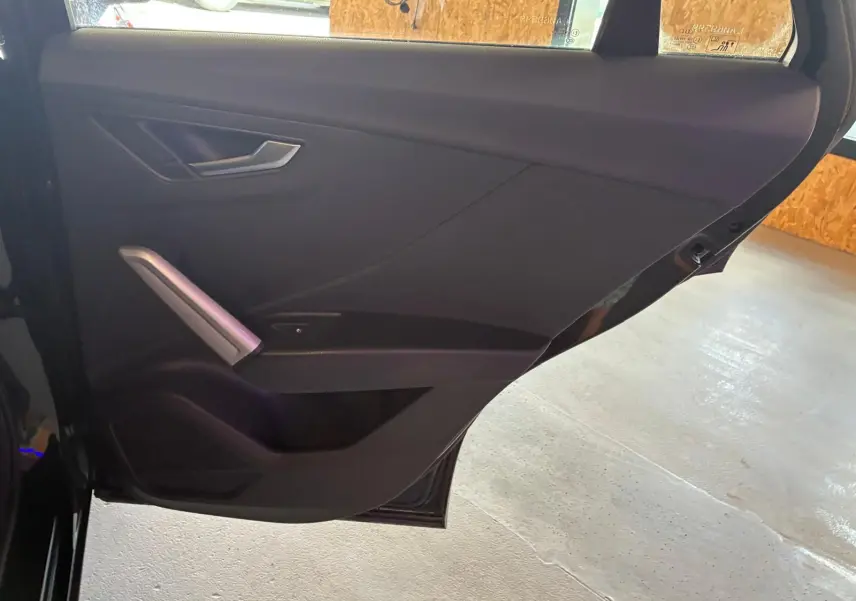 Vue intérieure de la porte arrière gauche noire d’un Audi Q2 30 1.6 TDI 2020 avec poignée argentée et garniture tissu noire.