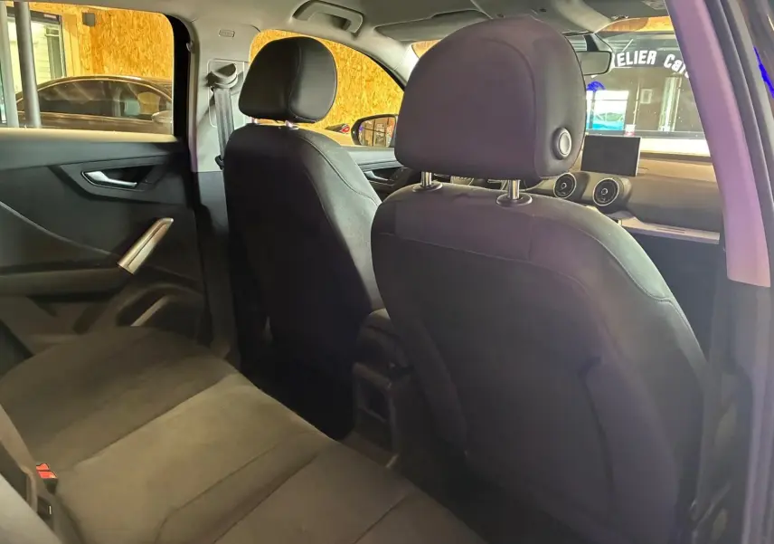 Vue intérieure arrière de l’Audi Q2 noire, montrant les sièges en tissu noir et le tableau de bord avec écran central.