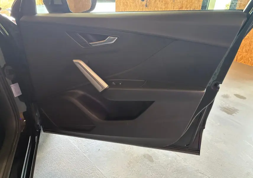 Vue intérieure de la porte côté gauche noire de l'Audi Q2 30 1.6 TDI 2020 avec poignée argentée et habillage tissu.