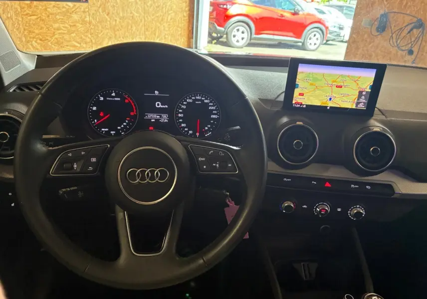 Vue intérieure centrée sur le volant noir d’un Audi Q2 2020 avec tableau de bord digital et écran GPS en surplomb.
