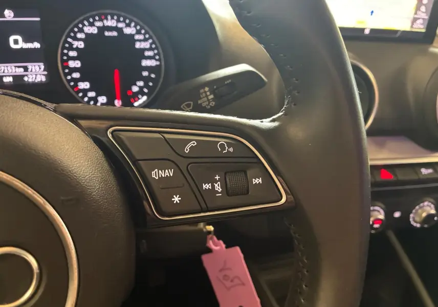 Gros plan sur le volant noir de l'Audi Q2 2020, avec commandes audio et tableau de bord lumineux en arrière-plan.