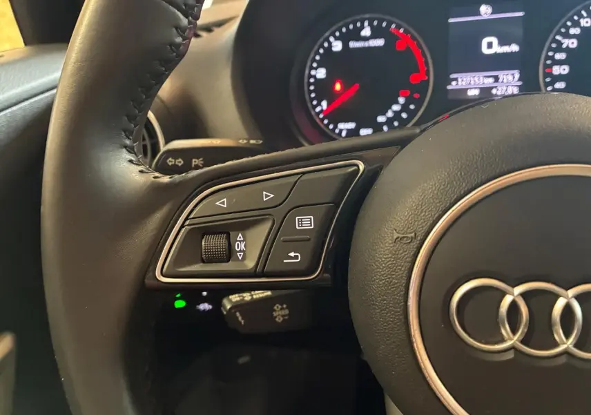 Gros plan sur le volant noir d’un Audi Q2 2020, montrant les commandes à gauche et le tableau de bord lumineux en arrière-plan.