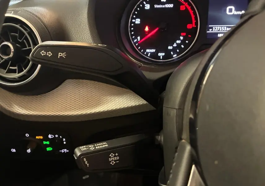 Gros plan sur le tableau de bord noir de l'Audi Q2 30 1.6 TDI 2020, avec compte-tours et commandes au volant visibles.
