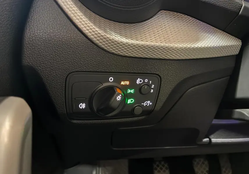 Gros plan sur le panneau de commande des phares de l’Audi Q2 30 1.6 TDI 116 BVM6 Design, intérieur noir.