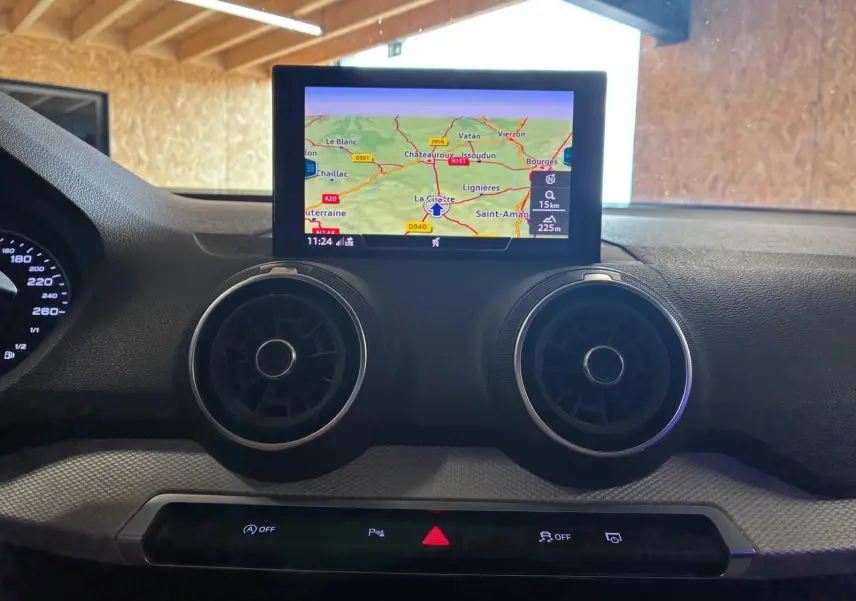 Vue intérieure centrée sur le tableau de bord noir de l'Audi Q2 2020, avec écran GPS et aérateurs ronds visibles.