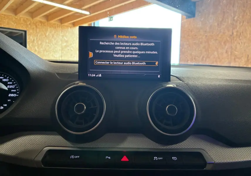 Vue rapprochée de la console centrale de l’Audi Q2 noire, avec écran multimédia et aérateurs ronds visibles.