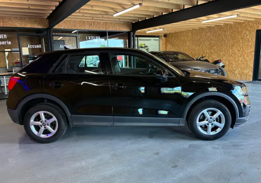 Audi Q2 noire vue de profil côté gauche dans un garage, soulignant ses jantes alliage et sa silhouette compacte.