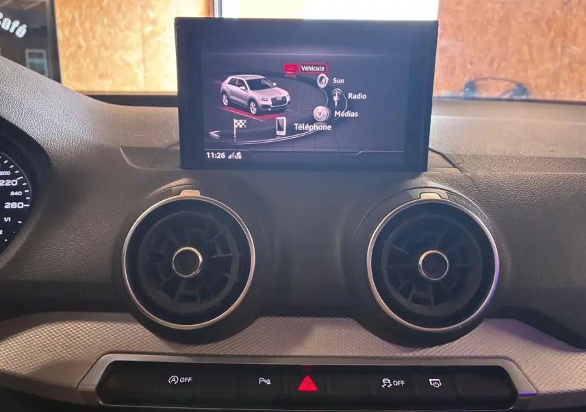Vue intérieure du tableau de bord de l'Audi Q2 noir 2020, avec écran central et aérateurs ronds visibles.