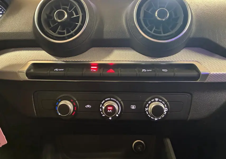 Vue rapprochée du tableau de bord noir de l'Audi Q2 2020, mettant en valeur les commandes de climatisation et les aérateurs ronds.