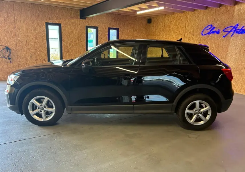 Audi Q2 noir vue de profil côté gauche dans un garage avec murs en bois et éclairage intérieur.