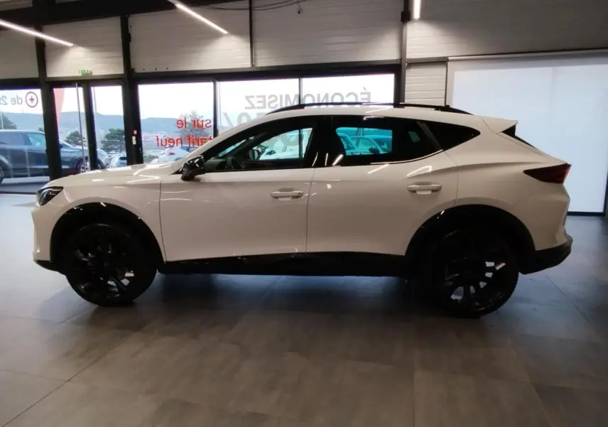 Vue de profil côté gauche d'un CUPRA Formentor blanc Nevada avec jantes noires en intérieur showroom.