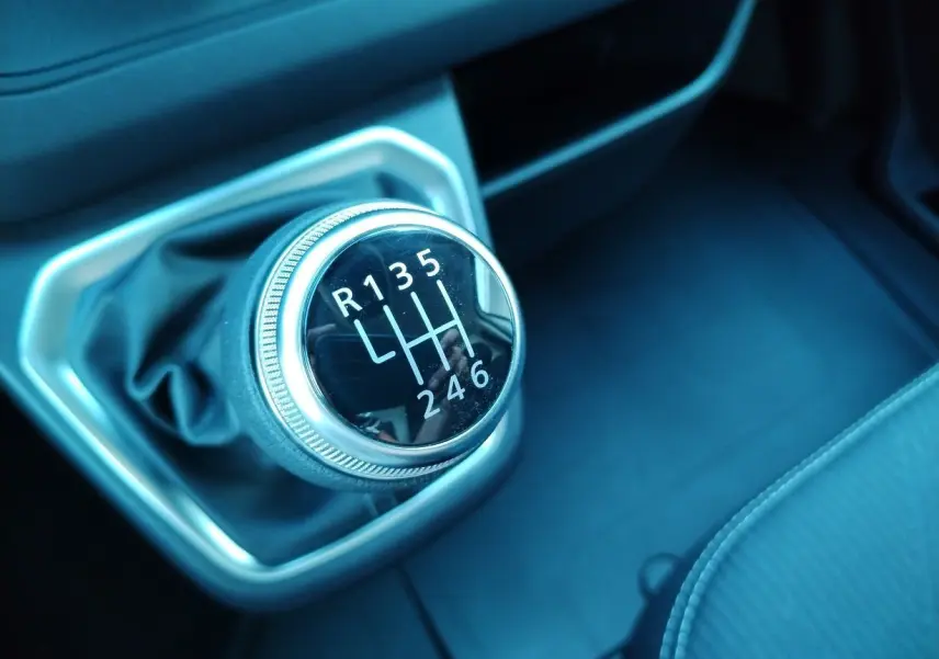 Gros plan sur le levier de vitesses manuel noir et chrome du Nissan Primastar blanc, intérieur sombre avec sellerie noire.