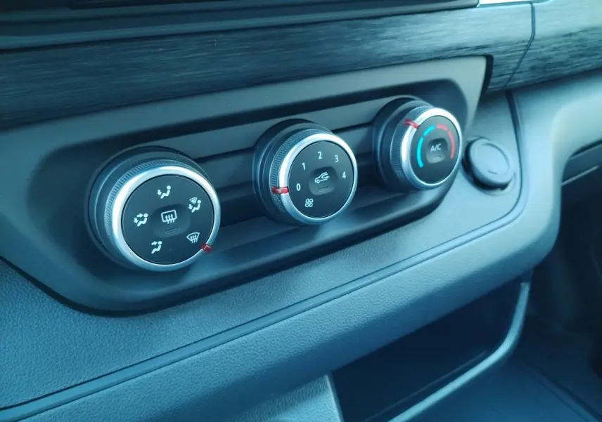 Gros plan sur les commandes de climatisation du tableau de bord du Nissan Primastar blanc 2025 avec pack bois.