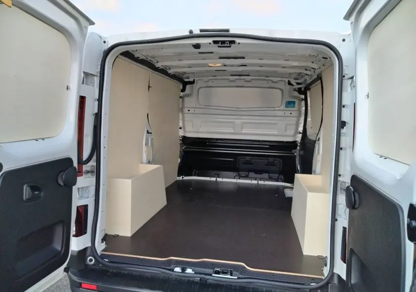 Vue arrière du Nissan Primastar blanc 2025 avec portes ouvertes montrant l'aménagement bois intérieur du coffre.