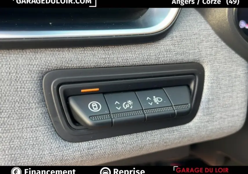 Gros plan sur les commandes de réglage des feux et verrouillage, tableau de bord tissu gris d’une Renault Clio noire.