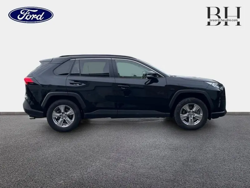 Profil latéral droit d'un Toyota RAV4 2.5 Hybride 2022 en noir Attitude métallisé avec jantes alu et barres de toit.