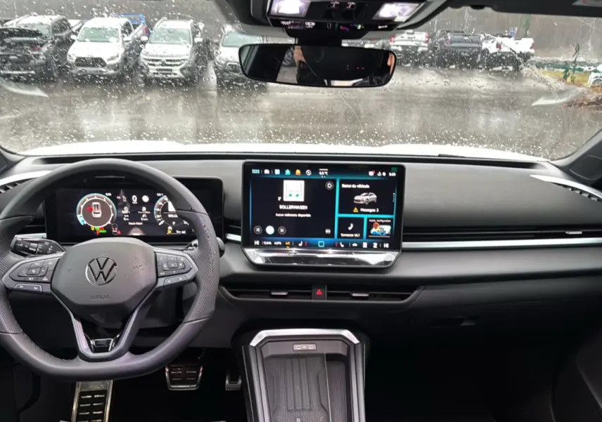 Vue intérieure frontale du tableau de bord du Volkswagen T-Roc blanc, avec écran tactile et volant multifonctions cuir.