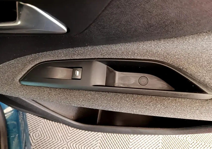 Gros plan sur la commande de lève-vitre côté gauche d’une Peugeot 3008 bleu, tissu gris et plastique noir.