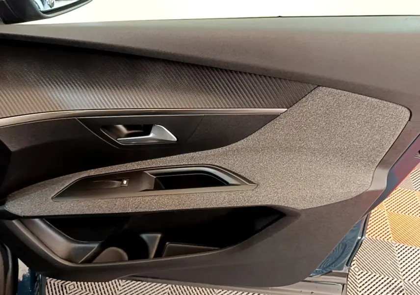 Vue intérieure de la porte avant gauche du Peugeot 3008 bleu, avec habillage tissu et insert imitation carbone.