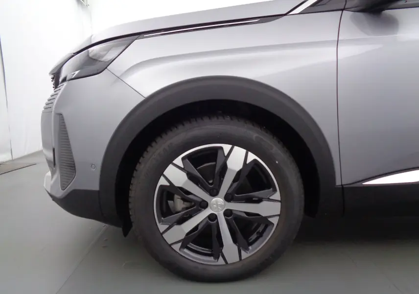 Gros plan sur la roue avant gauche d'un Peugeot 3008 gris Artense métal avec jante alliage bicolore.