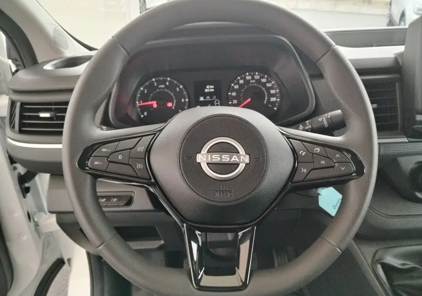 Vue centrée sur le volant noir du Nissan Primastar 2025, avec tableau de bord et commandes visibles en arrière-plan.