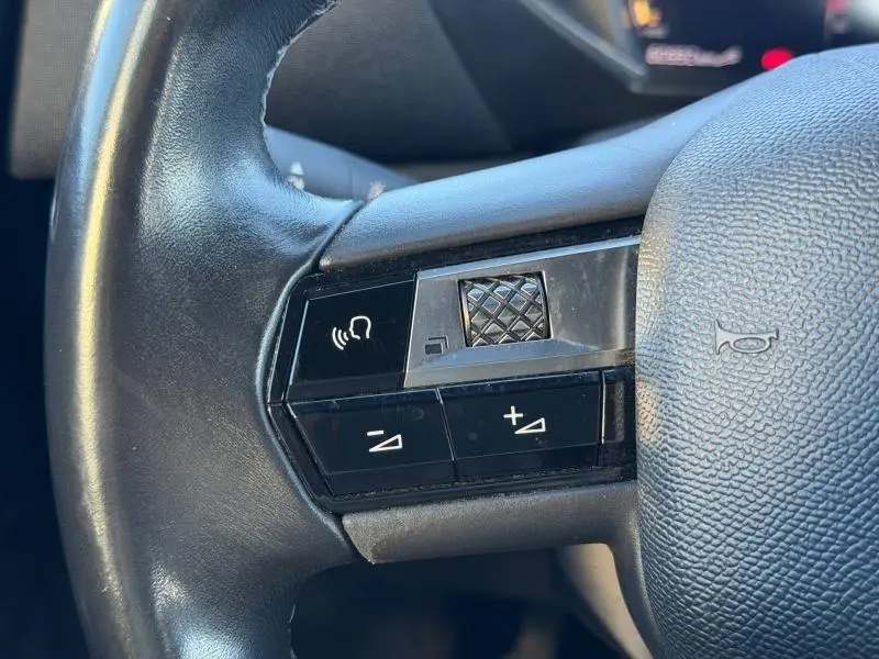 Gros plan sur les commandes gauche du volant noir du DS3 Crossback 2020 PureTech, avec molette et boutons de volume.