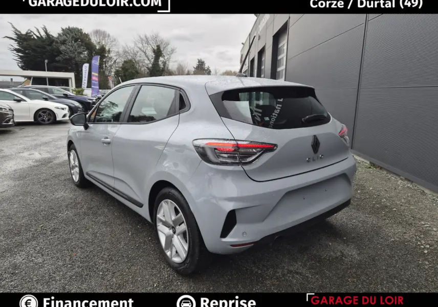 Vue 3/4 arrière droite d'une Renault Clio gris clair 2025 garée devant un bâtiment gris.